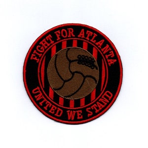 Könnte beinhalten: Ein runder schwarzer und roter Aufnäher mit dem Text "Fight for Atlanta United We Stand" in einem weißen Kreis um einen braunen Fußball mit schwarzen Nähten.
