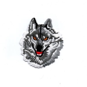 Könnte beinhalten: Gestickter Bügelaufkleber mit dem Kopf eines grauen Wolfes mit orangefarbenen Augen und einem roten Maul.