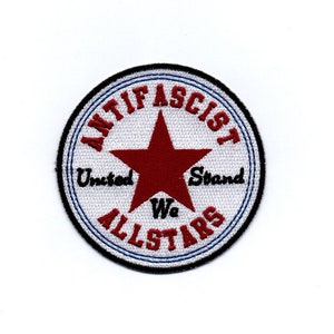 Könnte beinhalten: Ein weißer, runder Patch mit einem roten Stern in der Mitte. Der Text "Anti-Fascist Allstars" ist in einer schwarzen, kreisförmigen Schrift um den Stern herum geschrieben. Der Text "United We Stand" ist in Schwarz unter dem Stern geschrieben.
