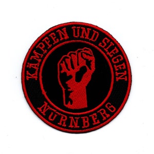 Puede incluir: Un parche bordado negro y rojo con un puño en alto y el texto "KÄMPFEN UND SIEGEN NÜRNBERG".
