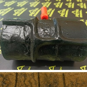 May include: A black rubber stamp with a textured surface, used to create a brick pattern. The stamp is being held by a red handle. The stamp is used to create a brick pattern on a surface.