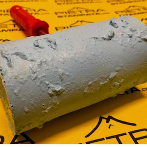 May include: A close-up of a textured roller used for applying decorative plaster. The roller is made of a light gray material and has a rough, uneven surface. The roller is lying on a yellow surface.