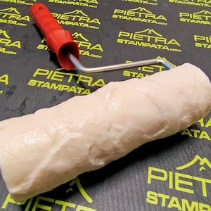 May include: A white textured roller with a red handle and a silver metal frame. The roller is used for creating a stone-like texture on walls.