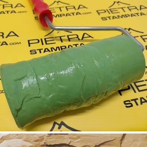 May include: A green rubber roller with a textured surface for creating a stone-like effect on walls. The roller is attached to a metal handle with a red plastic grip. The roller is on a yellow surface with the text "PIETRA STAMPATA" printed on it.