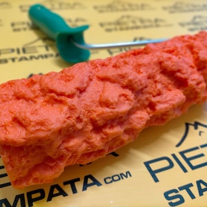 May include: Orange textured paint roller with a green handle. The roller is designed to create a stone-like effect on walls.