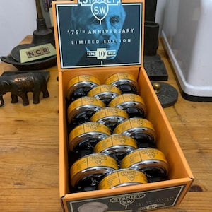 May include: A display box of Stanley S.W. 175th Anniversary Limited Edition 10' tape measures. The box is orange and black, with the Stanley logo and a portrait of a man. The tape measures have yellow and black casings.