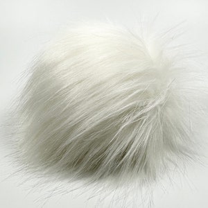 May include: A fluffy white pom pom made of faux fur. The pom pom is round and has a soft, plush texture.