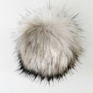 May include: A fluffy white pom pom with black tips. The pom pom is made of faux fur and is ideal for adding a touch of whimsy to any project.