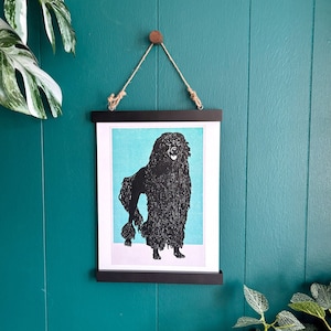 Może przedstawiać: Czarno-biała ilustracja pudla na niebieskim tle. Ilustracja jest oprawiona w czarną ramę i wisi na turkusowej ścianie.