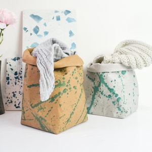 Könnte beinhalten: Zwei Stoffaufbewahrungskörbe mit grünem und blauem Farbspritzer-Design. Ein Korb ist braun und der andere weiß. Ein weißes Tuch befindet sich im braunen Korb.