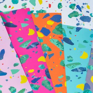May include: Five sheets of colorful paper with a terrazzo pattern. The papers are pink, orange, blue, gray, and white. The pattern is made up of small, irregular shapes in various colors, including blue, green, yellow, and red.