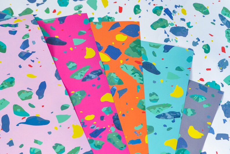 May include: Five sheets of colorful paper with a terrazzo pattern. The papers are pink, orange, blue, gray, and white. The pattern is made up of small, irregular shapes in various colors, including blue, green, yellow, and red.
