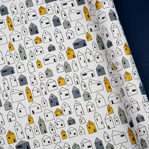 Op de afbeelding: Wit inpakpapier met een herhalend patroon van kleine huisjes in verschillende tinten blauw, grijs en geel. De huisjes zijn zwart omlijnd en hebben een eenvoudig, modern ontwerp.