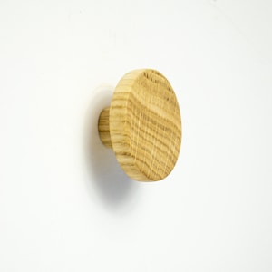 May include: A round wooden knob with a natural wood finish. The knob is attached to a wall.