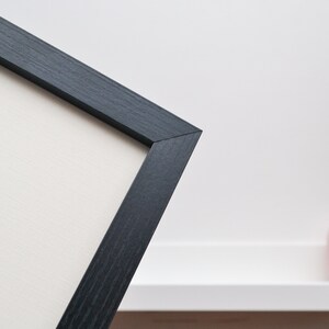 May include: Close-up of a black picture frame with a white mat. The frame is made of wood and has a simple, modern design.