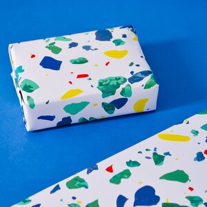 May include: A white gift box wrapped in colorful terrazzo patterned paper. The paper features blue, green, yellow, and red abstract shapes.