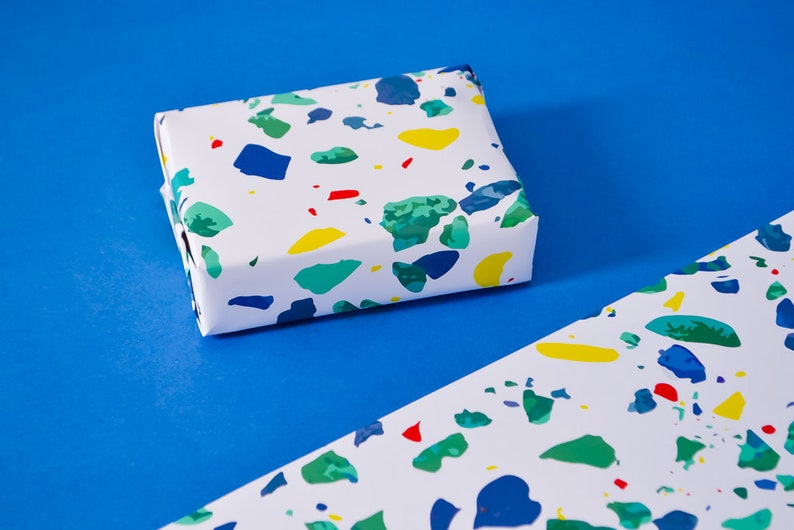 May include: A white gift box wrapped in colorful terrazzo patterned paper. The paper features blue, green, yellow, and red abstract shapes.