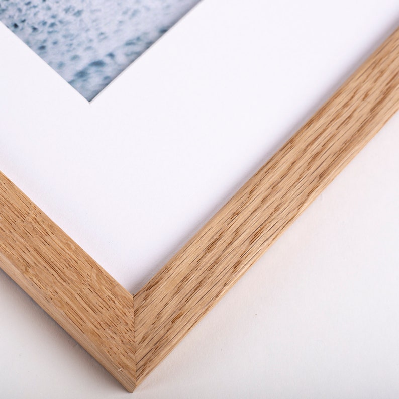 May include: Close-up of the corner of a natural wood picture frame. The frame is made of light brown wood with a visible grain pattern.