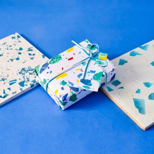May include: A white gift box with a colorful confetti pattern and a blue ribbon. The box is sitting on a blue surface.