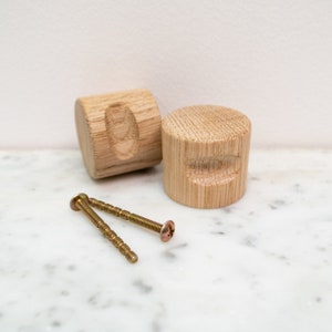 May include: Two wooden knobs with a rounded, cylindrical shape. The knobs are made of light brown wood and have a slightly textured surface. Two gold screws are included.