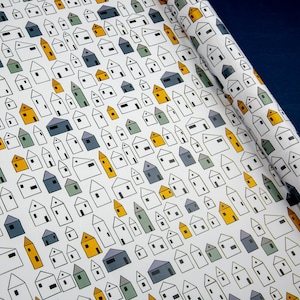 Op de afbeelding: Wit inpakpapier met een herhalend patroon van kleine huizen met zwarte contouren. De huizen zijn gevuld met gele, blauwe en groene kleuren.