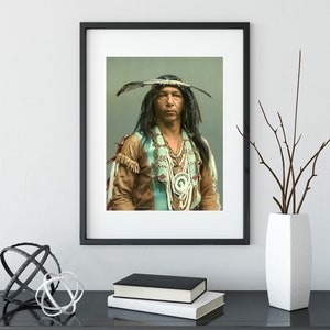 Puede incluir: Un retrato en blanco y negro de un hombre nativo americano con un tocado de plumas y ropa tradicional. Está mirando directamente a la cámara con una expresión seria.