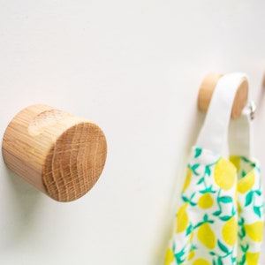 Może przedstawiać: Drewniany haczyk ścienny z naturalnym wykończeniem. Haczyk jest okrągły i ma gładką powierzchnię. Jest zamontowany na białej ścianie.