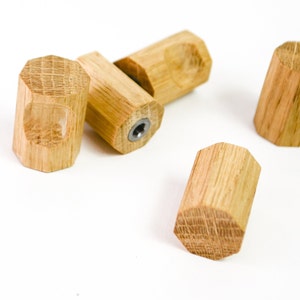 Puede incluir: Cuatro pomos de armario de madera con forma hexagonal. Los pomos son de madera marrón claro con un patrón de veta natural.