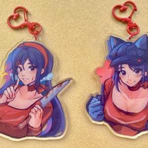 May include: Two acrylic keychains featuring anime-style illustrations of women. One holds a bloody knife, the other wears a hat. Both have red heart-shaped clasps. The women are wearing red tops and blue hair.