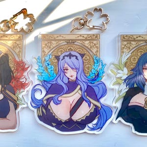 May include: Three acrylic keychains with anime-style illustrations of female characters. Each keychain has a gold floral charm and a detailed portrait with floral accents. The characters are depicted in various outfits and hairstyles.