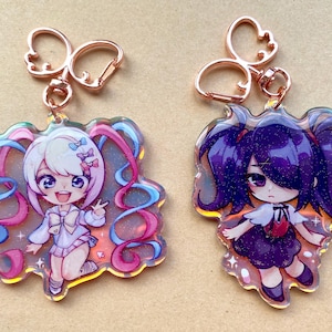 May include: Two anime-style acrylic keychains. One features a character with white hair and pink and blue accents, the other with purple hair. Both have rose gold-colored key rings.