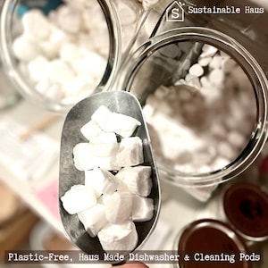 May include: White dishwasher detergent pods in a glass jar and a metal scoop. The jar has a label that says "Sustainable Haus". The text "Plastic-Free, Haus Made Dishwasher & Cleaning Pods" is at the bottom of the image.