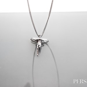 Könnte beinhalten: Silberne Kettenkette mit einem Anhänger einer geflügelten Engelsfigur.