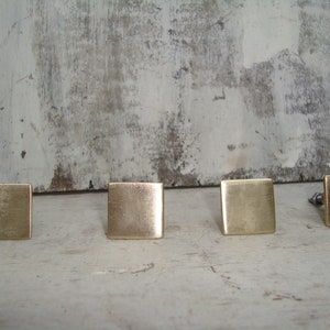 May include: Four square brass cabinet knobs with a brushed finish.