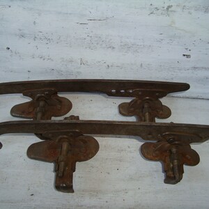 May include: A pair of vintage rusty metal ice skate blades. The blades are attached to a metal frame with a screw and a metal plate. The blades are in good condition, but show signs of wear and tear.