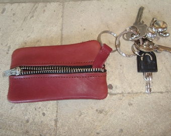 May include: A burgundy leather key chain with a zipper closure. The keychain is attached to a set of keys with a silver ring.