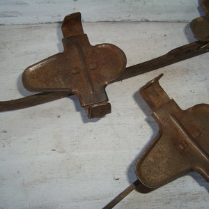 May include: A set of three rusty metal ice skate attachments. The attachments are designed to be attached to the bottom of shoes to provide traction on ice.