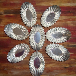 May include: Eight silver-coloured metal baking cups with fluted edges arranged in a starburst pattern on a wooden surface.