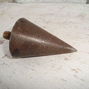 May include: A vintage metal plumb bob with a wooden handle. The plumb bob is a cone shape with a pointed tip. It is a tool used for leveling and measuring.