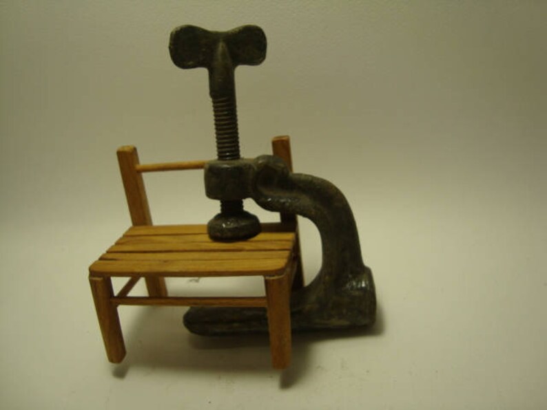 May include: A vintage metal clamp with a wooden handle, attached to a small wooden chair. The clamp has a screw mechanism and a metal handle.