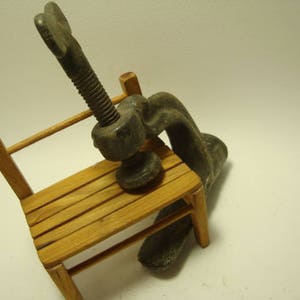 May include: A vintage metal clamp with a wooden base. The clamp is made of metal and has a screw mechanism. The base is made of wood and has a natural finish.