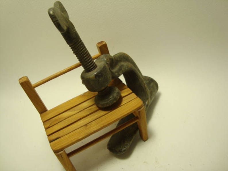 May include: A vintage metal clamp with a wooden base. The clamp is made of metal and has a screw mechanism. The base is made of wood and has a natural finish.