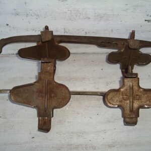 May include: A pair of vintage ice skates with metal blades and rusty brown metal frames. The skates have a simple design with a cross-shaped foot strap and a single buckle.