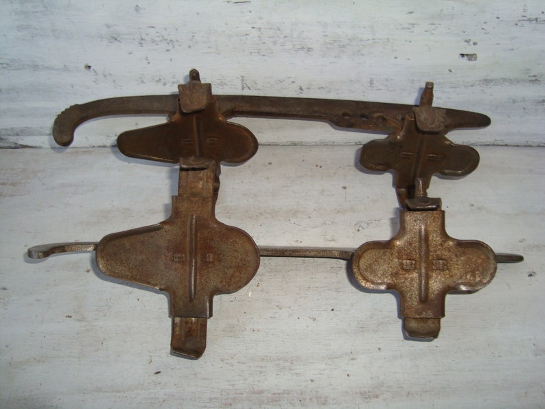 May include: A pair of vintage ice skates with metal blades and rusty brown metal frames. The skates have a simple design with a cross-shaped foot strap and a single buckle.