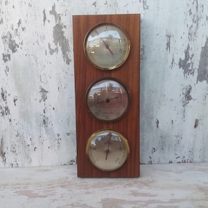 May include: A vintage wooden wall-mounted barometer with three round analog gauges. The gauges have gold-colored bezels and measure temperature, humidity, and barometric pressure.