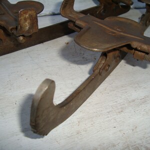 May include: A pair of vintage ice skates with metal blades and a rusty brown finish. The skates have a simple design with a single strap and buckle.