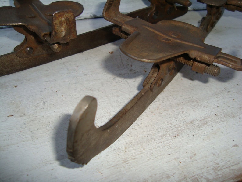 May include: A pair of vintage ice skates with metal blades and a rusty brown finish. The skates have a simple design with a single strap and buckle.