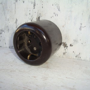 Puede incluir: Una tapa de toma de corriente eléctrica de baquelita marrón oscuro con tres agujeros para cables.