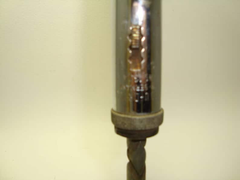 May include: A silver and chrome hand drill with a metal bit. The drill has a textured grip and a metal handle.