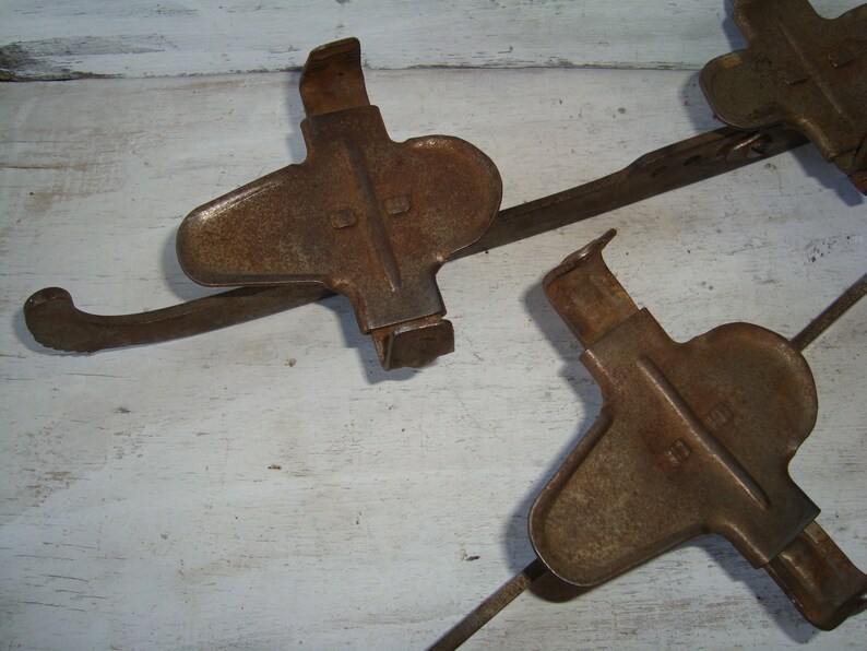 May include: A set of three rusty metal ice skate attachments. The attachments are connected by a metal bar and have a curved shape with a pointed end.